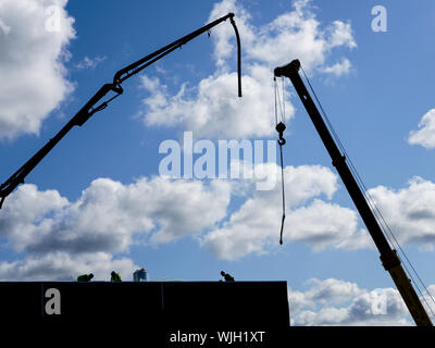 elevated crane booms on a construction site, against a blue sky Stock Photo