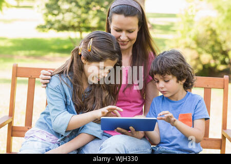 Smiling woman with kids using digital tablet on park bench Stock Photo