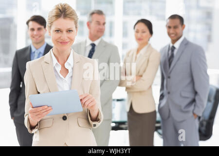 Happy businesswoman using her tablet with team behind her in the office Stock Photo