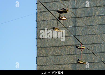 Several tennis shoes on power lines in front of a clear blue sky. Stock Photo