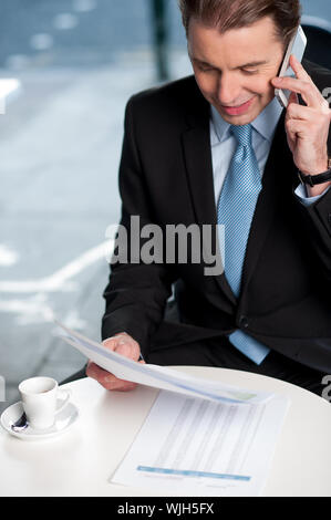Corporate guy communicating on phone with reports in hand Stock Photo