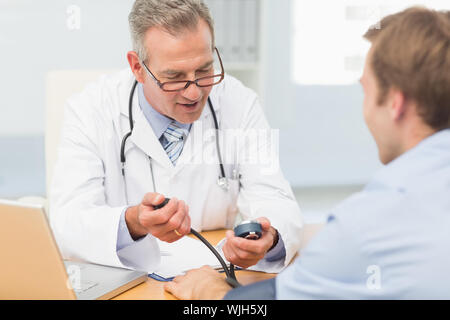 Happy doctor taking his patients blood pressure in his office at the hospital Stock Photo