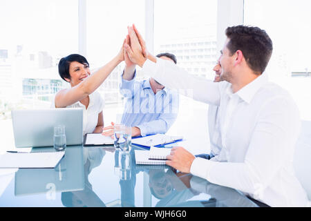 Smartly dressed young executives giving high five in a business meeting at office desk Stock Photo