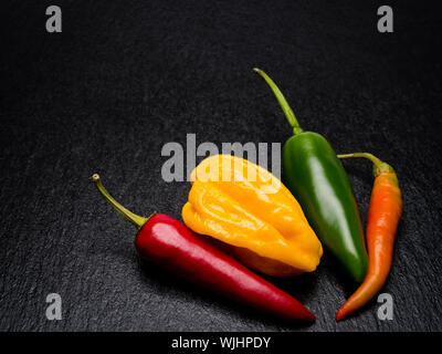 Three different chili peppers on black slate. Stock Photo