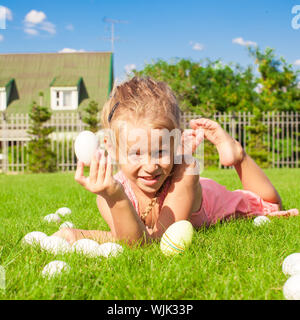 Little beautiful girl finds Easter eggs on green grass Stock Photo