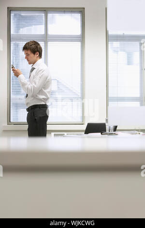 Side view of a young businessman sending text message by desk in office Stock Photo