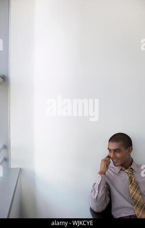 Smiling mixed race businessman using mobile phone in office against the wall Stock Photo