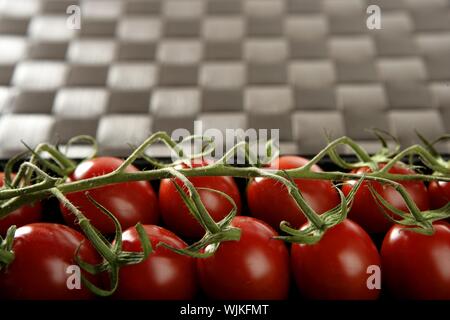 Red tomatoes branch un a black plastic box over brown tablecloth Stock Photo