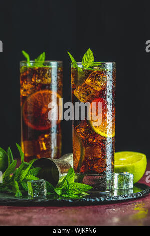 Cold Longdrink Cuba Libre with brown rum and fresh lime in highball glass with water drops on dark background, selective focus Stock Photo