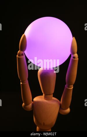 wooden mannequin holding a pink light ball over head Stock Photo