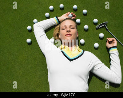 Beautiful female golfer lying on putting green with golf balls and club Stock Photo