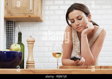 Young woman text messaging through cellphone while leaning on wooden counter in kitchen Stock Photo