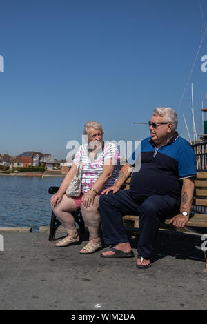 An overweight middle aged couple sitting on a park bench Stock Photo
