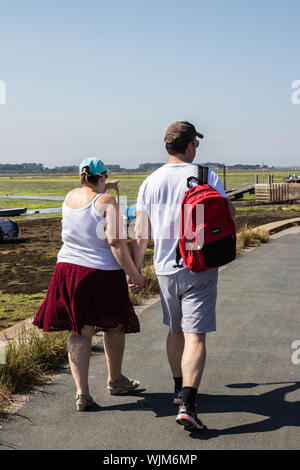 A middle aged couple holding hands walking along a shoreline in summer Stock Photo