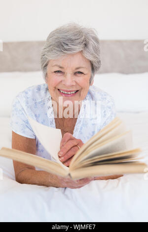 Portrait of happy senior woman turning story book pages in bed at home Stock Photo