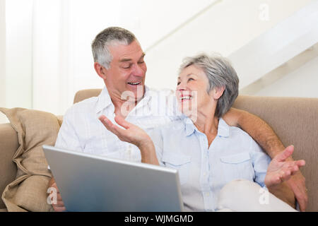 Loving senior couple with laptop looking at each other on sofa at home Stock Photo