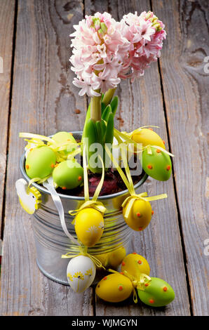 Arrangement of Pink Hyacinth in Tin Bucket and Multi Colored Spotted Easter Eggs with Ribbons closeup on Rustic Wooden background Stock Photo
