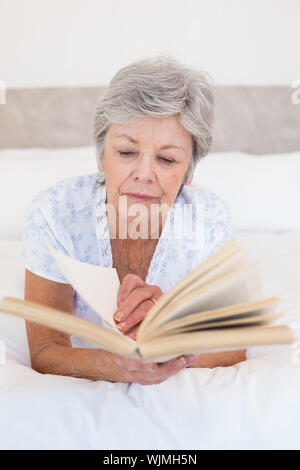 Concentrated senior woman reading story book in bed Stock Photo