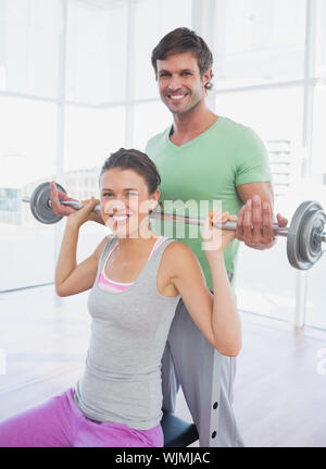 Male instructor helping fit woman to lift barbell in the gym Stock Photo