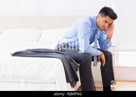 Frowning businessman sitting at edge of bed at home in bedroom Stock Photo