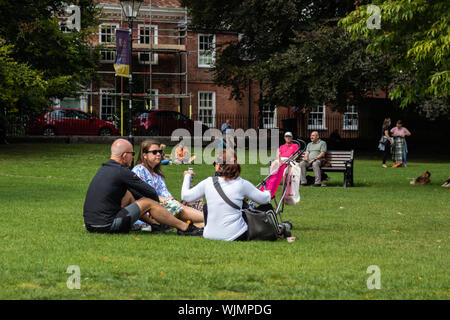 people sat in the park on the grass enjoying the sunshine on a summers day Stock Photo