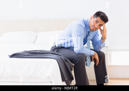 Frowning businessman sitting at edge of bed looking at camera at home in bedroom Stock Photo
