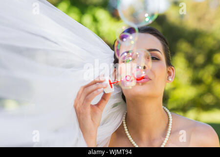 Cheerful young beautiful bride blowing soap bubbles in the park Stock Photo