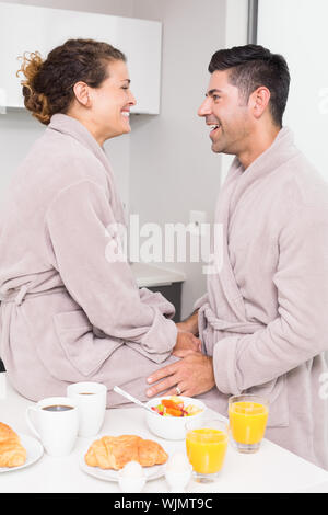 Happy couple in bathrobes having breakfast together at home in kitchen Stock Photo