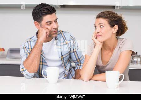Fed up couple having coffee looking at each other at home in kitchen Stock Photo