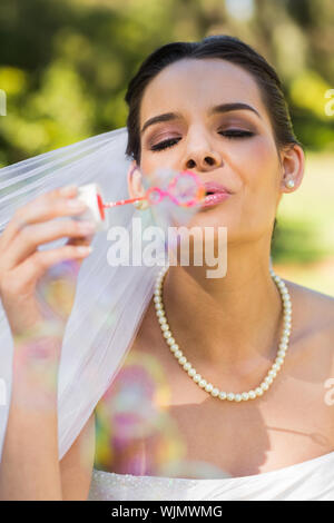 Close-up of a young beautiful bride blowing soap bubbles in the park Stock Photo