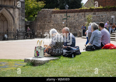 Winchester, Hampshire, UK an elderly couple sat on a wall in the park enjoying lunch in the sunshine Stock Photo