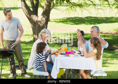 Father at barbecue grill with extended family having lunch in the park Stock Photo