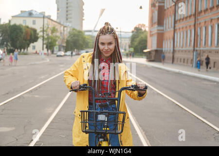 Portrait of pretty girl in yellow coat sitting on bike