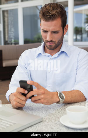 Frowning businessman sending a text at table in patio of restaurant Stock Photo