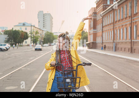 Portrait of pretty girl in yellow coat raised hand sitting on bike Stock Photo