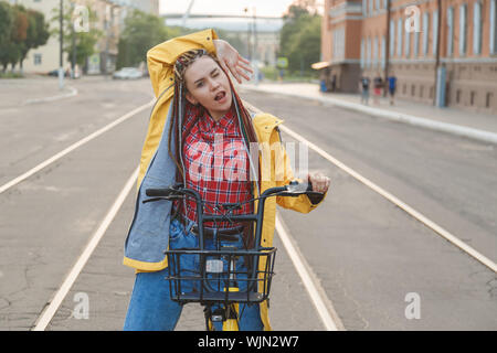 Portrait of pretty girl in yellow coat raised hand sitting on bike
