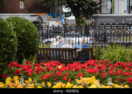 Three middle aged women sat on a wooden bench in the park surrounded by flowers Stock Photo