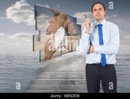 Thinking businessman holding pen against bridge in ocean under cloudy sky Stock Photo