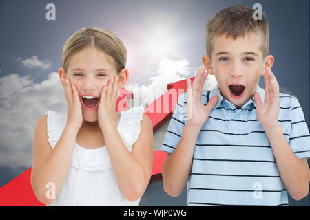 Brother and sister being shocked against red arrows pointing against sky Stock Photo