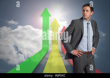 Serious businessman with hands on hips against colorful arrows pointing up against sky Stock Photo