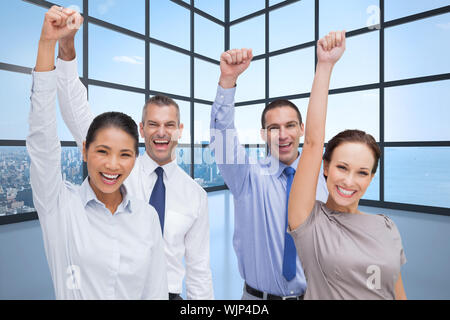 Cheerful work team posing with hands up against room with large window showing city Stock Photo