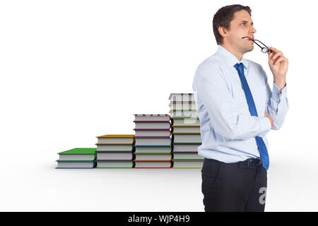 Thinking businessman biting glasses against steps made from books Stock Photo
