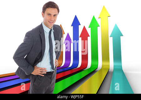 Cheerful businessman standing with hands on hips against colourful arrows pointing up Stock Photo