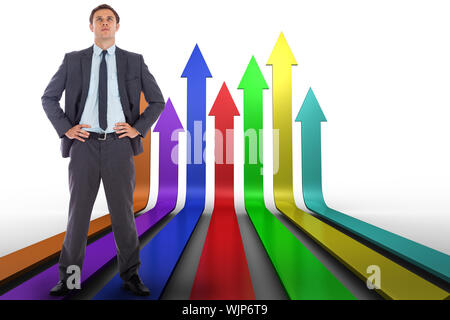 Serious businessman with hands on hips against colourful arrows pointing up Stock Photo