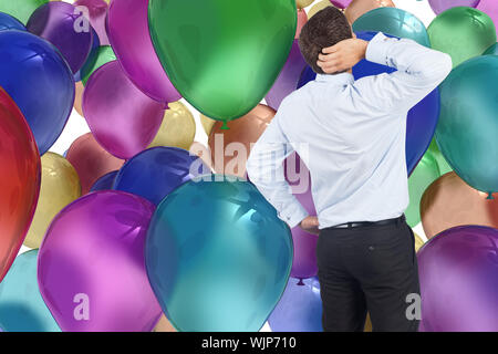 Thinking businessman scratching head against colourful balloons Stock Photo