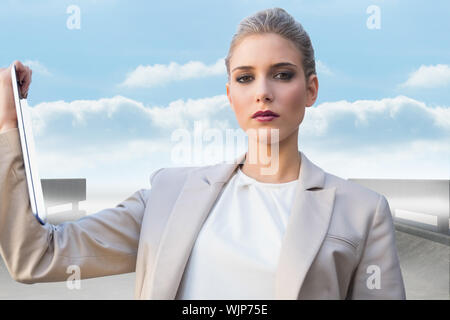 Serious classy businesswoman holding tablet  against road leading out to the horizon Stock Photo