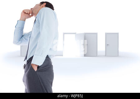 Thoughtful businessman with hand on chin against door opening revealing bright light Stock Photo