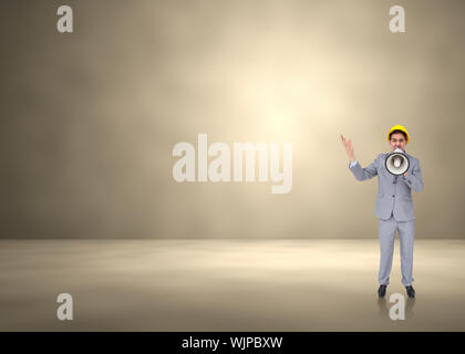 Architect with hard hat shouting with a megaphone against grey room Stock Photo