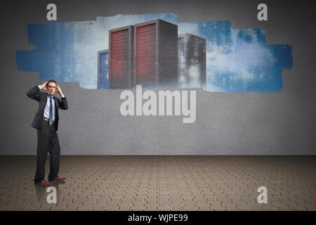 Stressed businessman with hands on head against display on wall showing server towers Stock Photo