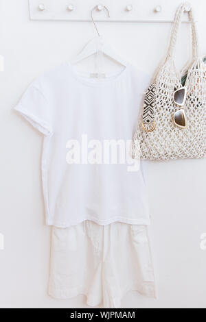 White clothes on a hanger in a locker room with a knitted string bag and sunglasses and a belt. Shopper and white things. Stock Photo